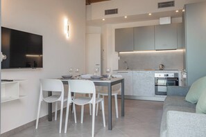 A modern kitchen with built-in appliances, a dining area with white chairs, and a grey sofa. - LUXURY 17C - Porto - Piscina - Jacuzzi (Santo Stefano al Mare)