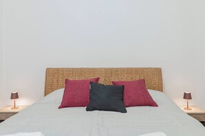 Ein Bett mit einem gewobenen Kopfteil, zwei Nachttischlampen und drei Kissen.