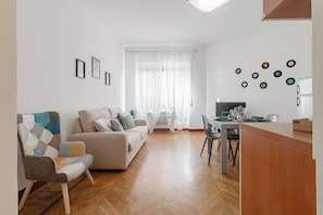Ein modernes Wohnzimmer mit einer Couch, einem Esstisch mit Stühlen und einer Küchenzeile mit Kühlschrank.