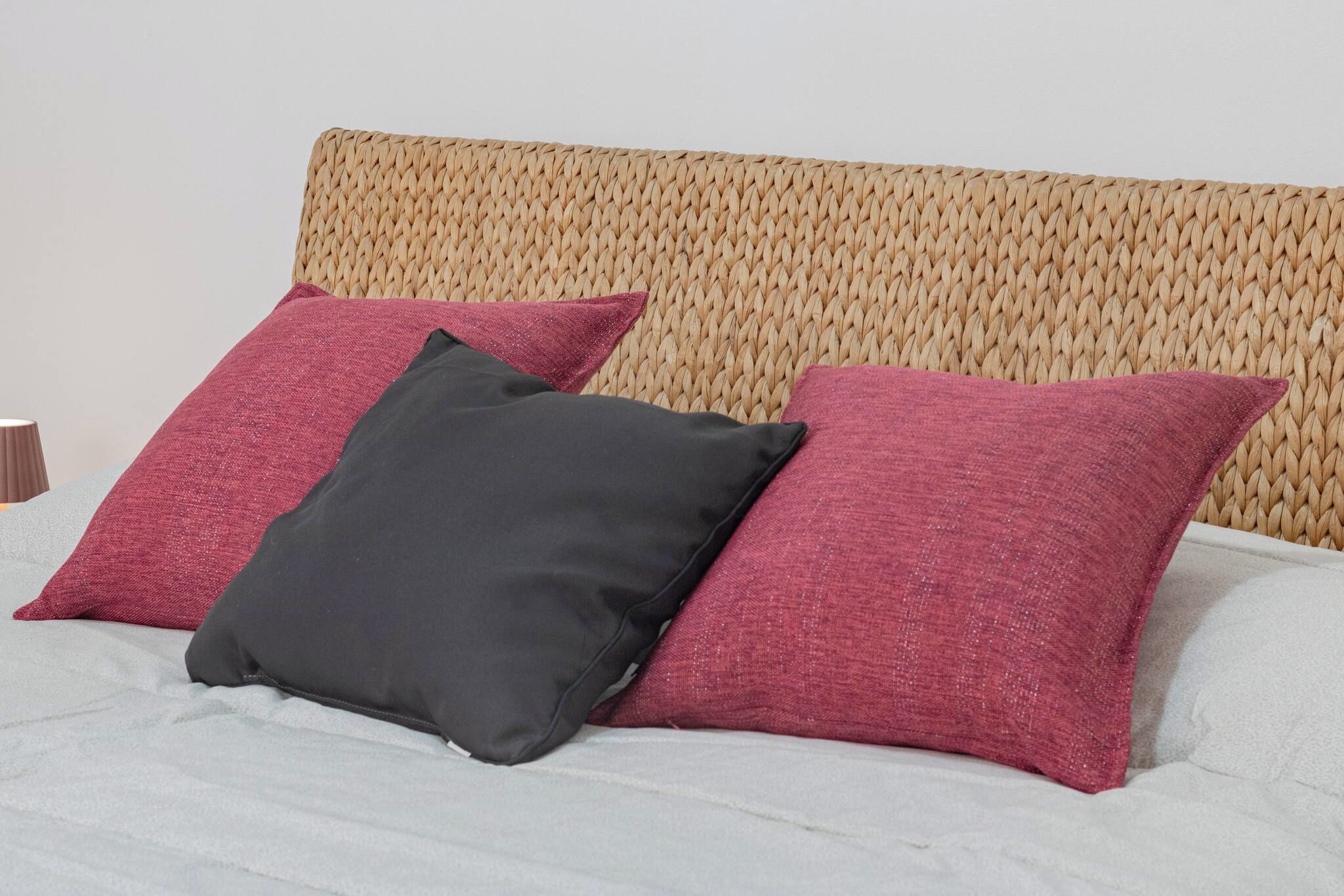 Un lit avec une tête de lit en osier et trois oreillers de couleurs différentes.