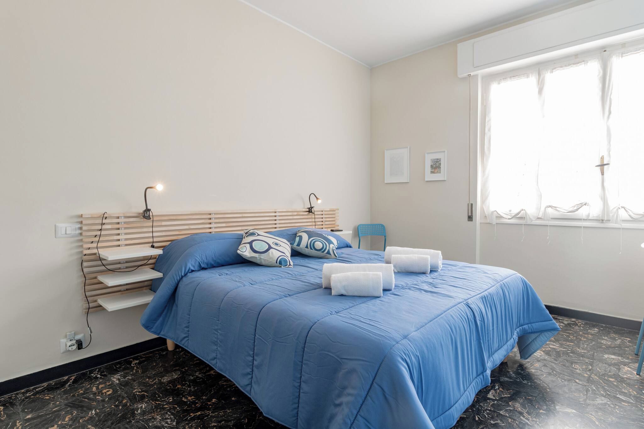 A bedroom with a bed, bedside lamps, a chair, a window, and artwork on the wall.