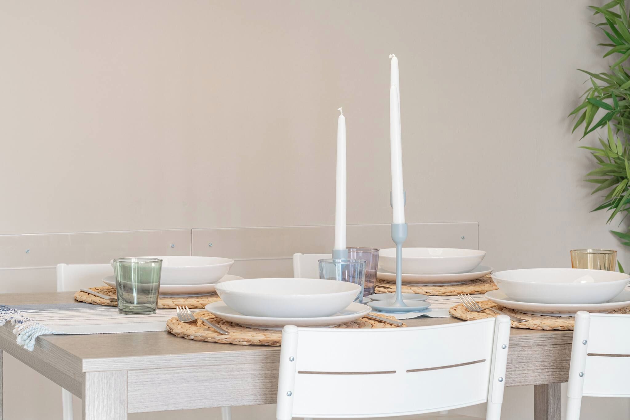 Mesa de comedor dispuesta con platos, tazones y un candelabro blancos.
