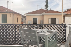 Een balkon met een tafel en stoelen, een versierd hekwerk en gebouwen met rode pannendaken op de achtergrond.