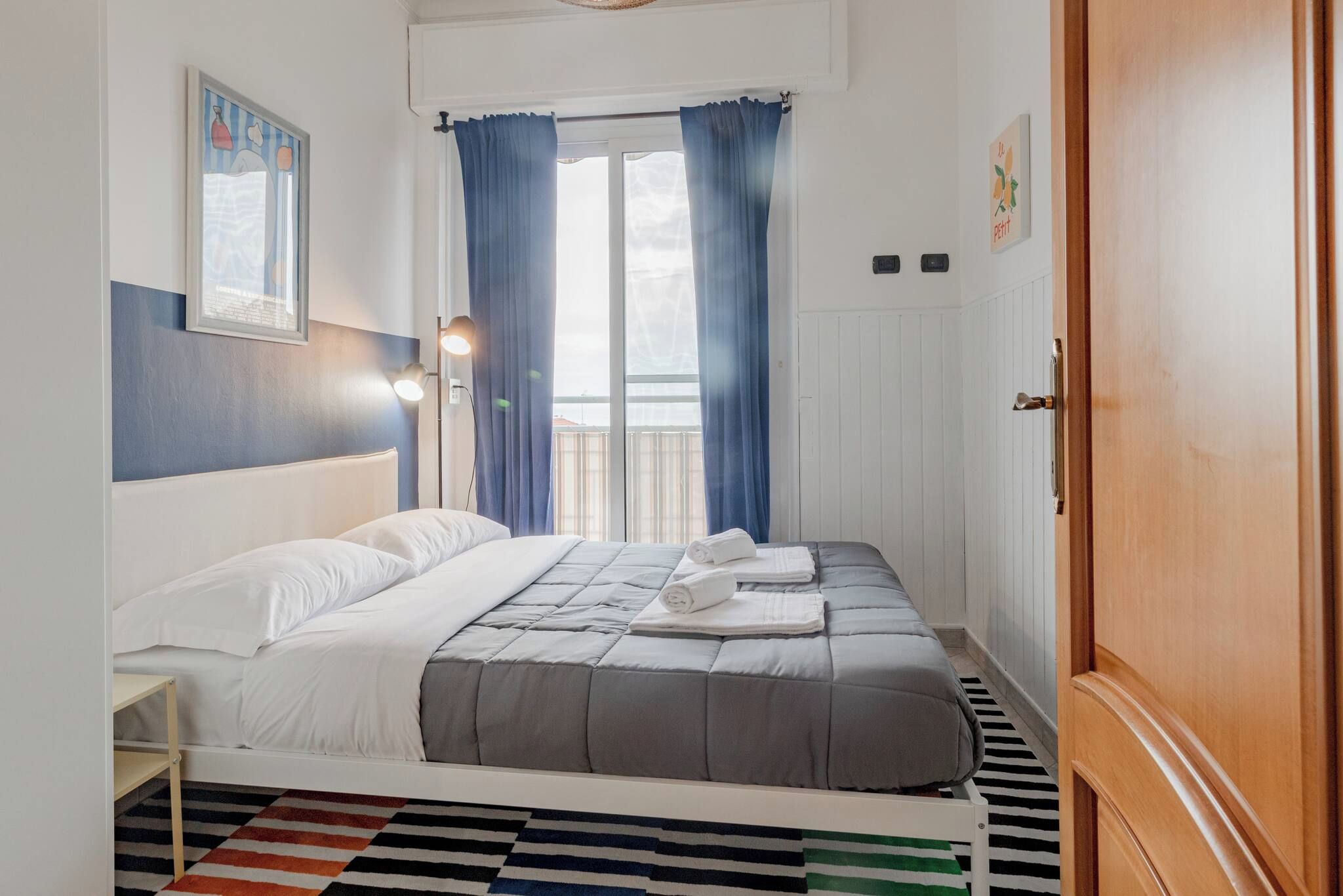 A bedroom with a bed, a nightstand, a window with curtains, and a door.