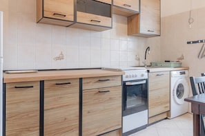 A modern kitchen with wooden cabinets, a built-in oven, a washing machine, and a tiled backsplash. - APPARTAMENTO AZUL - Centro Sanremo (Sanremo)