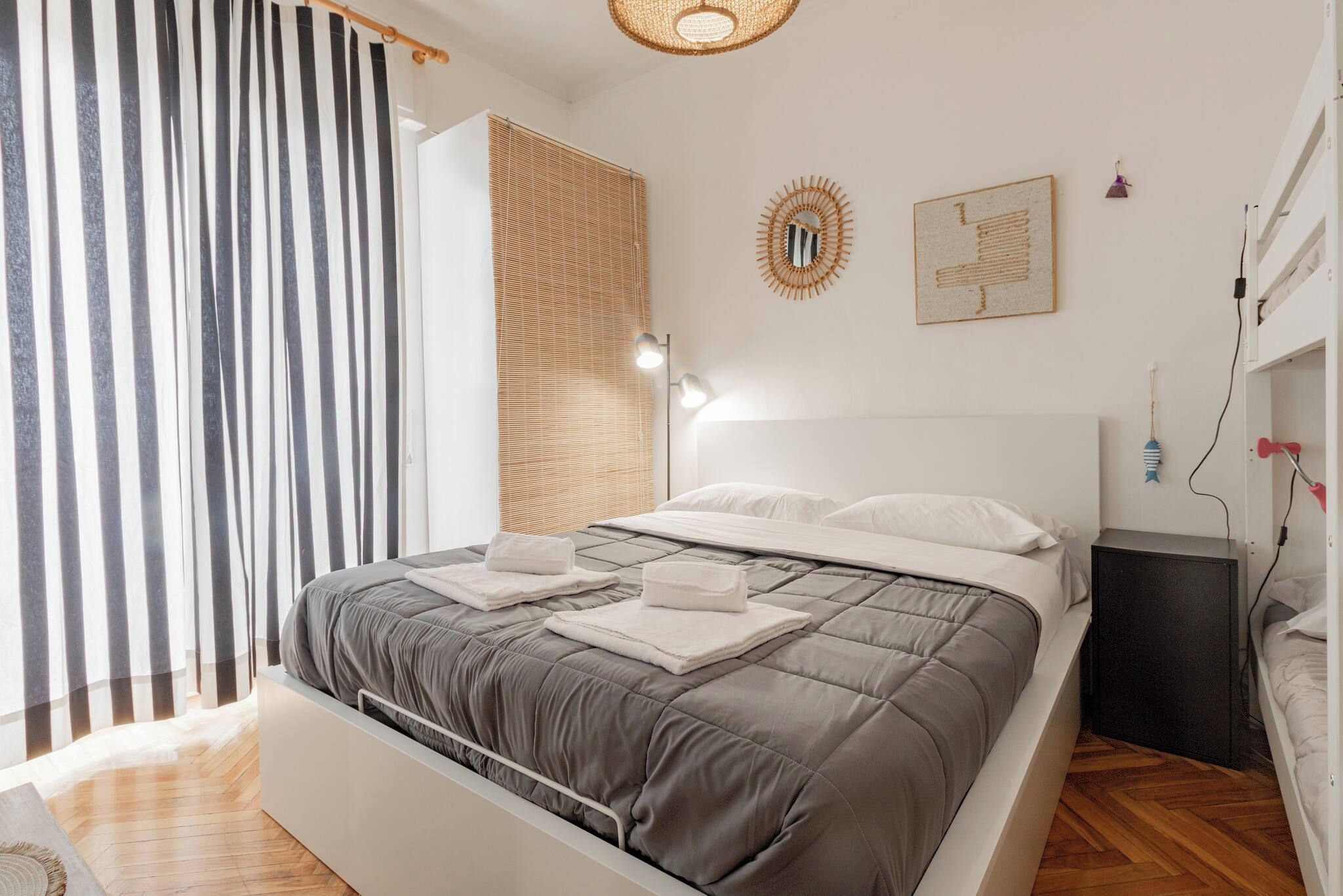 Une chambre moderne avec un lit, des tables de chevet, une lampe fixée au mur et une fenêtre avec des stores.