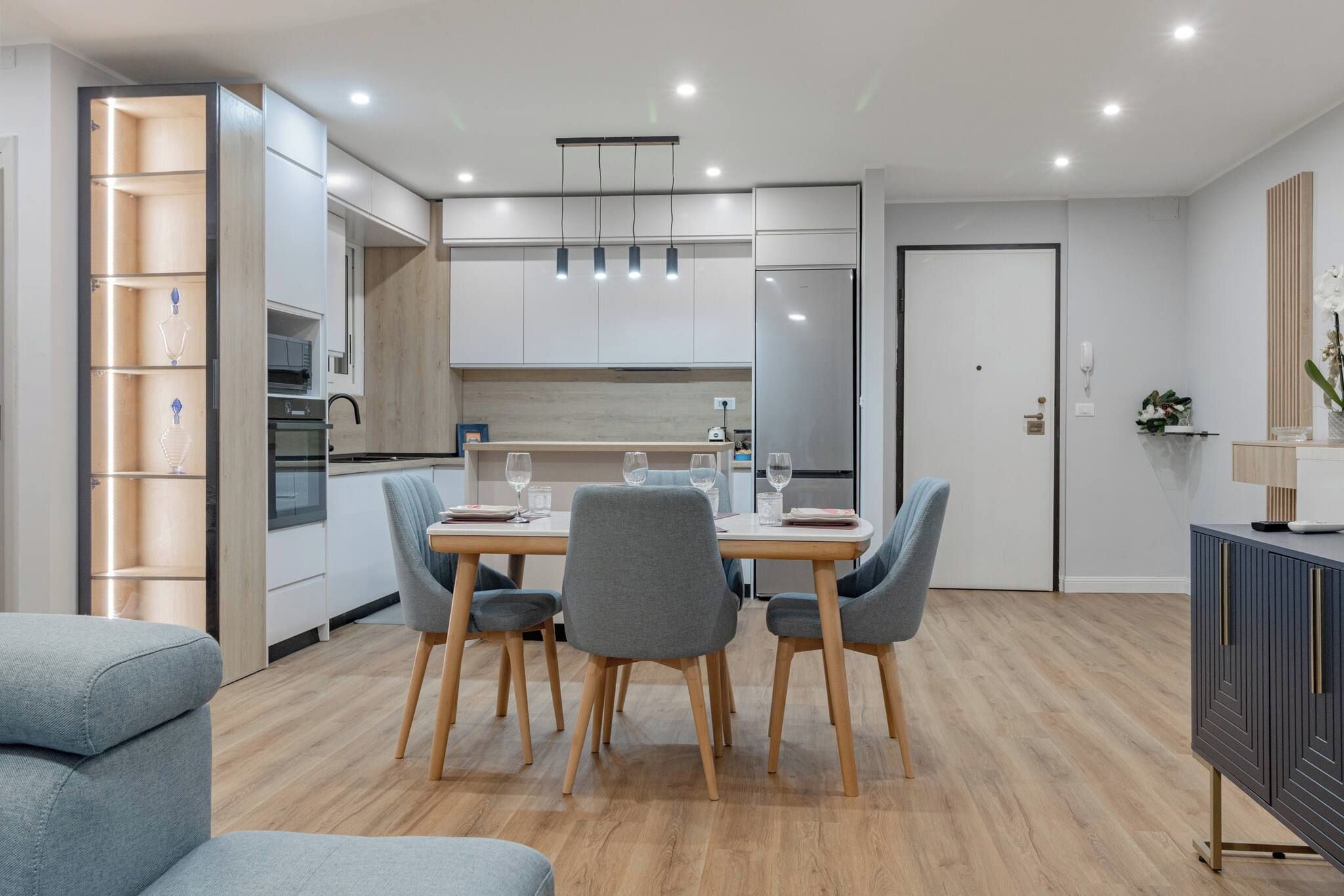 A modern kitchen with white cabinets, a dining table with four chairs, and a built-in oven.