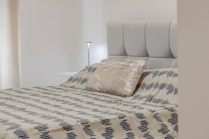 A bed with a patterned bedspread and two pillows, a bedside table, and a floor lamp. - CASA GIGLIO - Parcheggio (Sanremo)