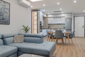 A modern living room with a grey sectional sofa, a dining table with chairs, and a kitchen area with white cabinets and a refrigerator. - CASA GIGLIO - Parcheggio (Sanremo)