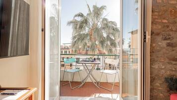 A balcony with a table and chairs, a TV on the left, and a stone wall on the right.
