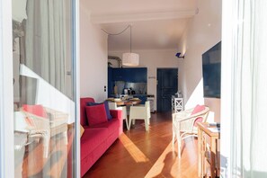 Ein modernes Interieur mit einem roten Sofa, Korbstühlen, einem Esstisch und einer Küchenzeile.