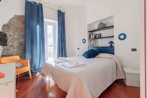 Ein Schlafzimmer mit einem Bett, einem Schreibtisch, einem Stuhl, einer Steinwand und einem Fenster mit Vorhängen.