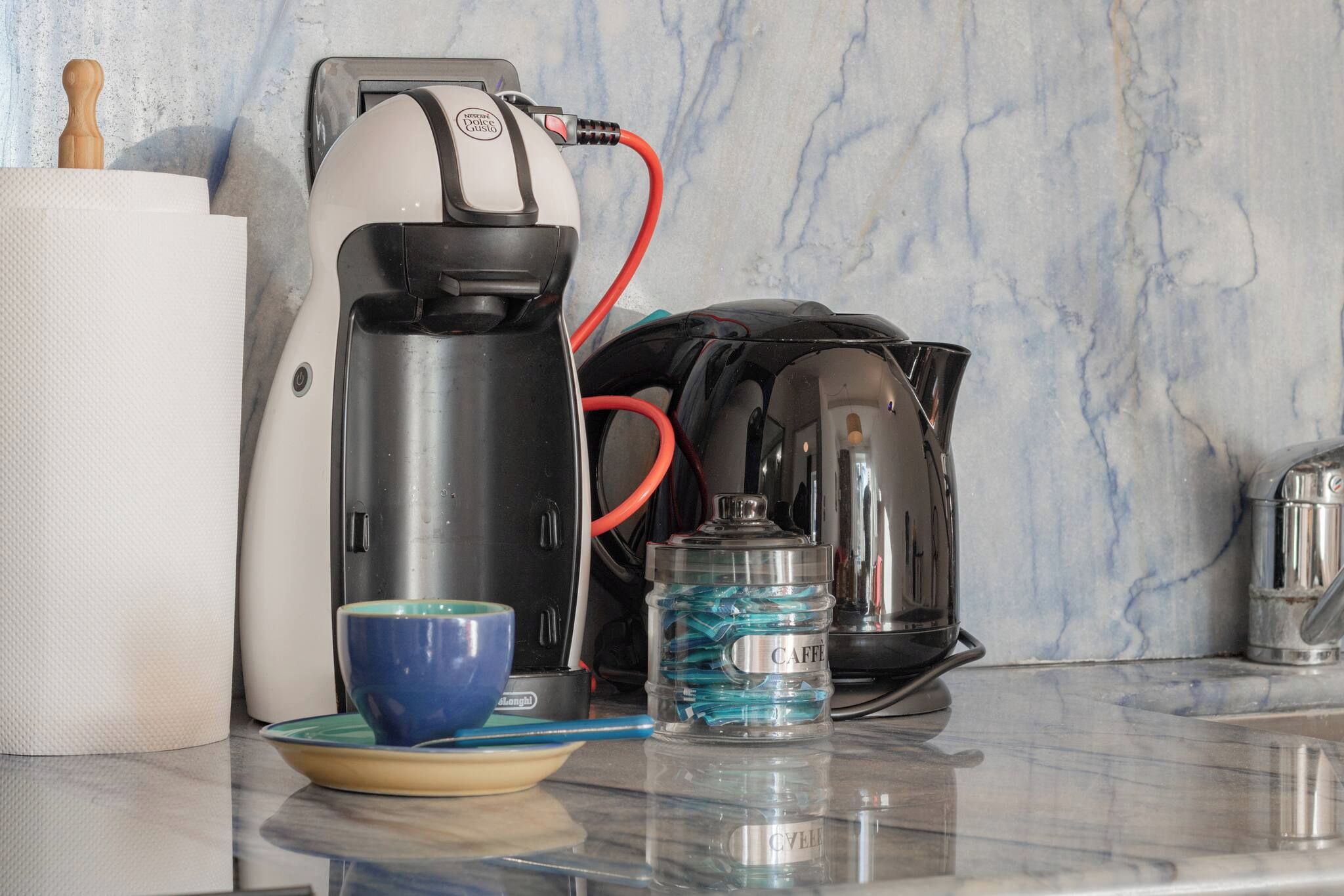 Un piano di lavoro in cucina con una macchina del caffè, una tazza, una bottiglia d'acqua e un bollitore.