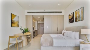 Una habitación de hotel moderna con cama, mesita de noche, lámpara y vista al área de la cocina.