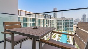 Un balcón con una mesa y sillas de madera, con vista a una piscina y edificios modernos.