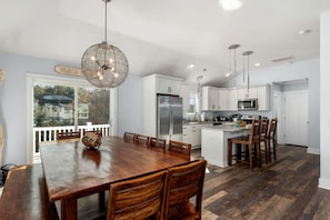 A modern kitchen with white cabinets, a stainless steel refrigerator, and a dining area with a wooden table and chairs. - Luxury Coastal Escape with Private Pool, BBQ Grill & Family Amenities in Corolla, North Carolina (Corolla)