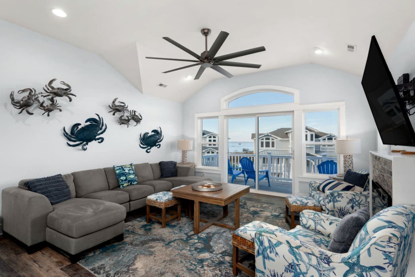 Un salón con un sofá gris, una mesa de centro de madera y vistas al océano a través de amplios ventanales.