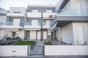 Un immeuble résidentiel moderne à plusieurs étages, doté de balcons, d’un espace extérieur couvert aménagé en coin salon et d’une entrée sécurisée par un portail.