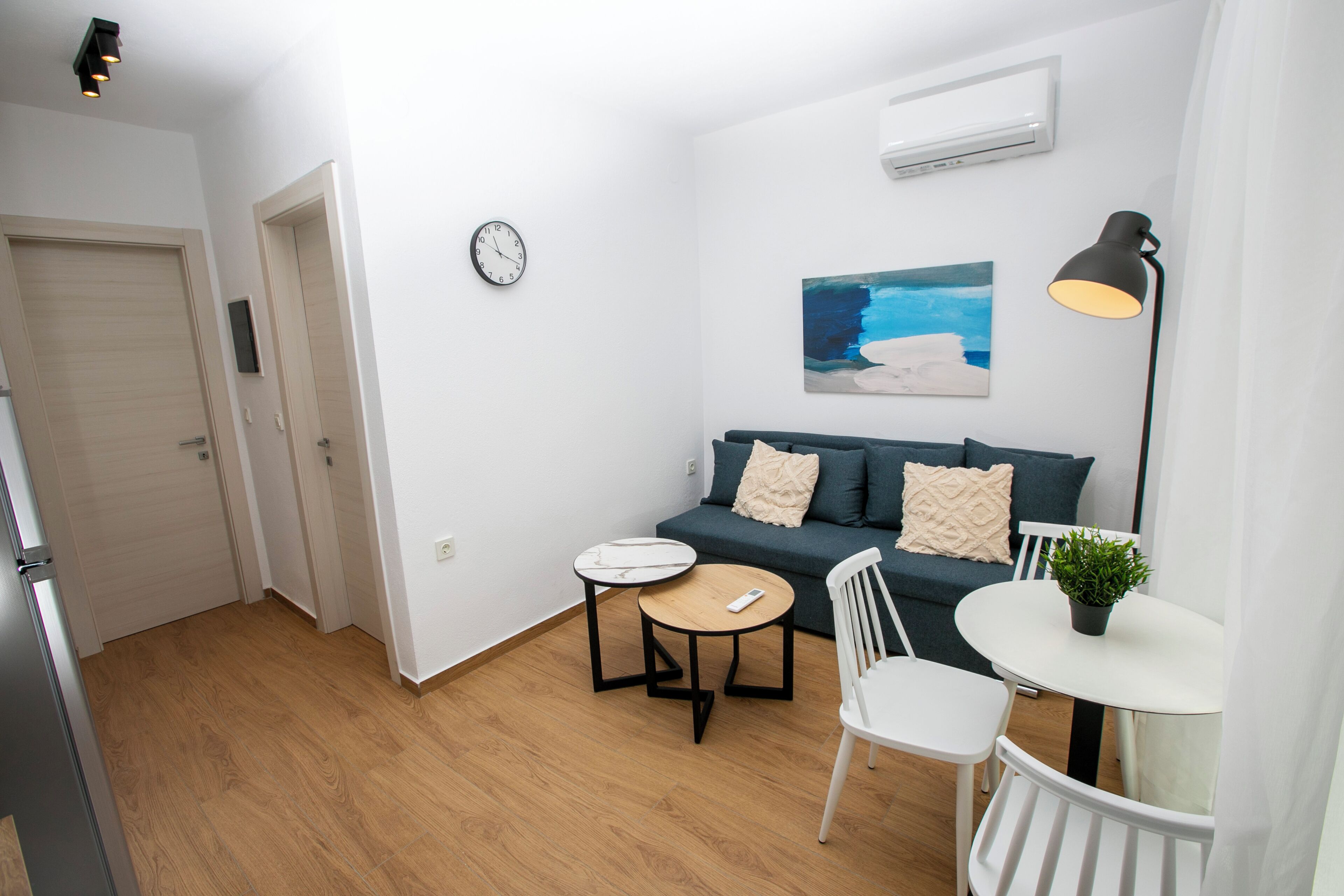 A compact living space with a sofa, two tables, a chair, a clock, and a painting on the wall.