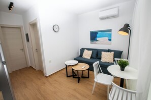 Un espace de vie compact comprenant un canapé, deux tables, une chaise, une horloge et un tableau accroché au mur.