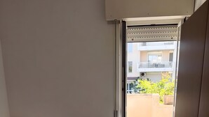 A room with two beds, a sliding door leading to an outdoor area, and a view of a building in the background.
