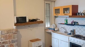 A compact kitchen with a microwave, oven, and a small table with a suitcase.