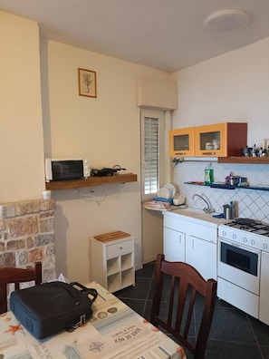A compact kitchen with a microwave, oven, and a small table with a suitcase.