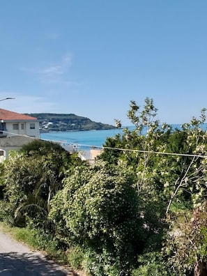 A coastal view with a road, greenery, and a distant hill.