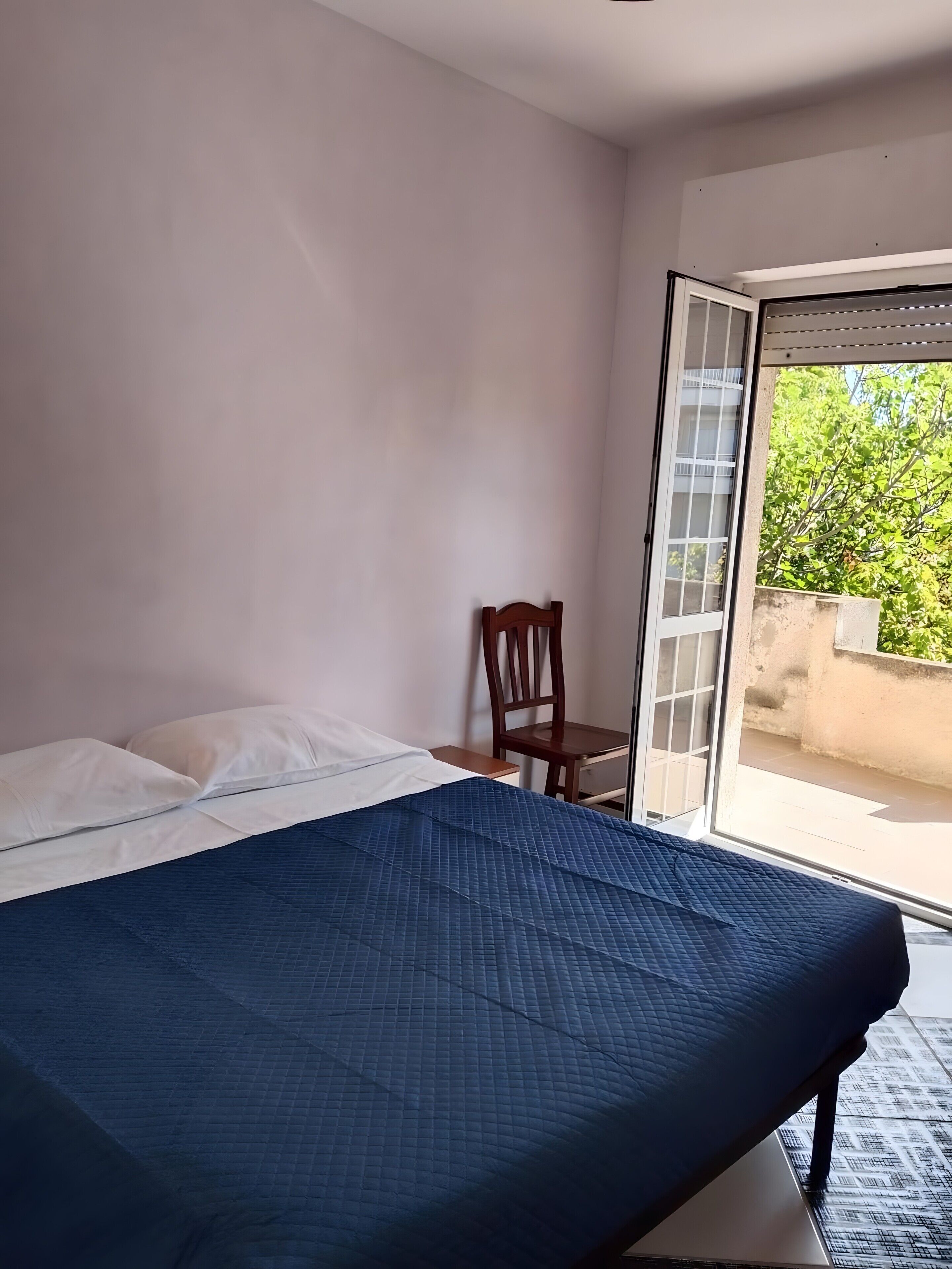 A bedroom with a bed, a chair, a window, and a view of greenery outside.