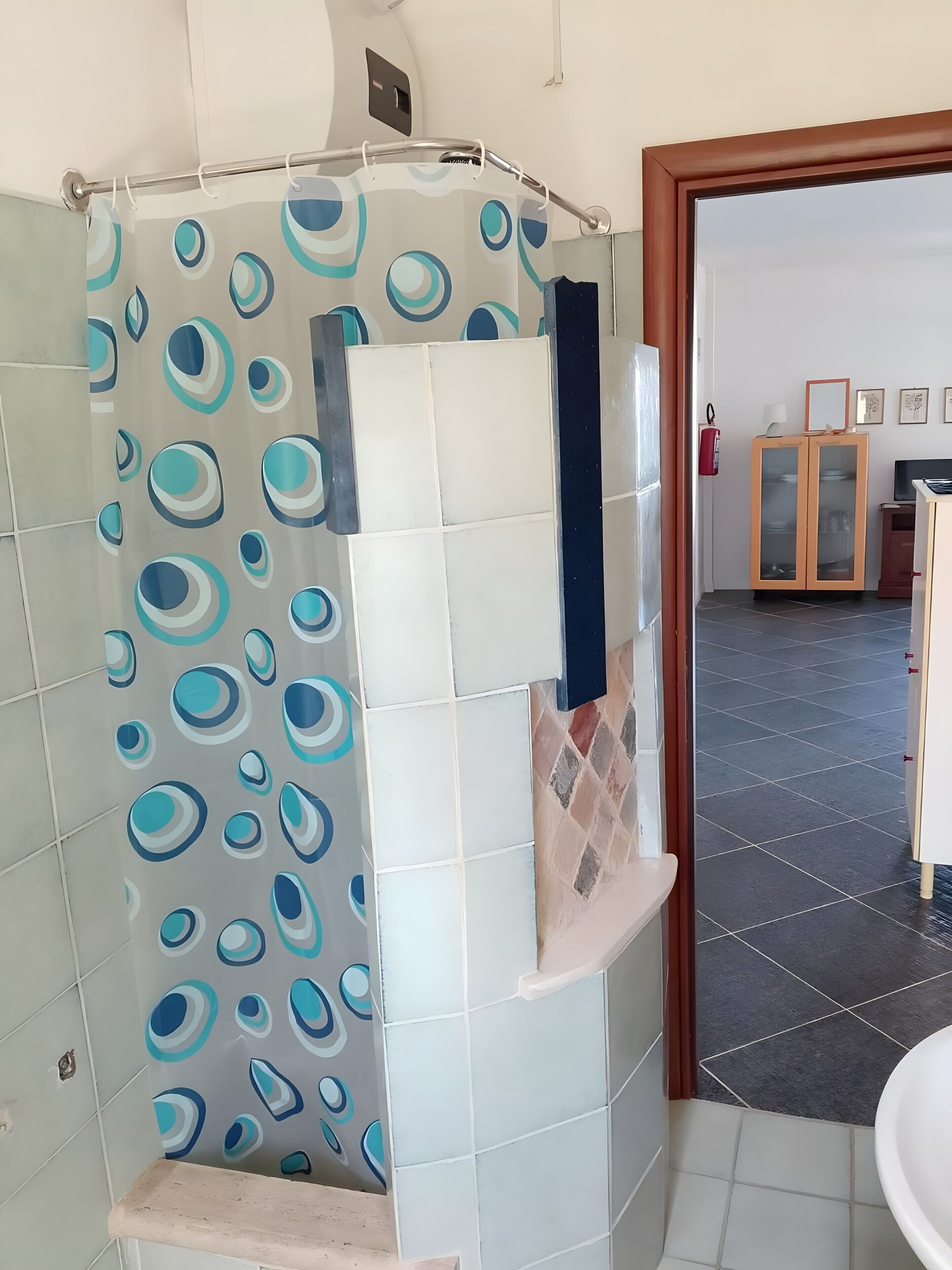 Une salle de bain avec un rideau de douche orné de motifs circulaires, un mur carrelé, un lavabo et un meuble avec des portes en verre.