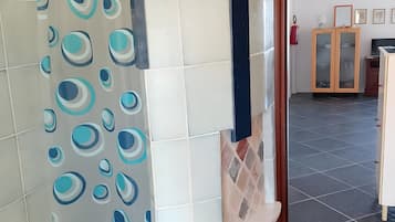 Une salle de bain avec un rideau de douche orné de motifs circulaires, un mur carrelé, un lavabo et un meuble avec des portes en verre.