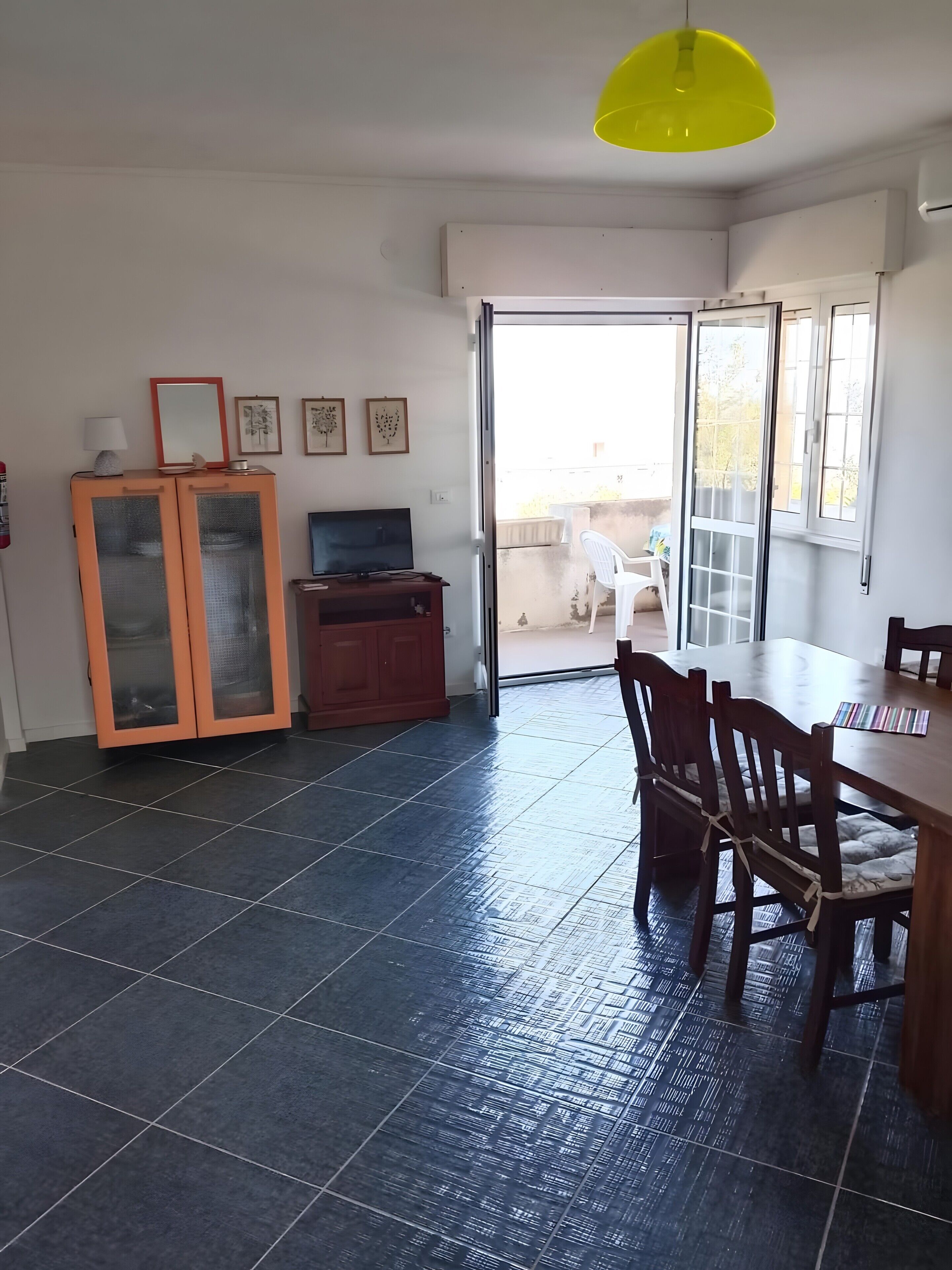 A room with a dining table, chairs, a TV, a cabinet, and a sliding glass door leading to an outdoor area.