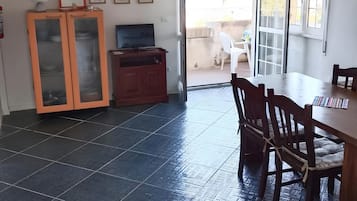 A room with a dining table, chairs, a TV, a cabinet, and a sliding glass door leading to an outdoor area.