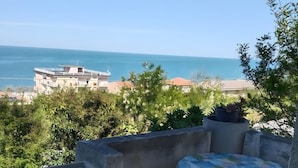 Ein Balkon mit Tisch und Stühlen, der auf eine Küstenlandschaft mit Gebäuden und Grünflächen blickt.