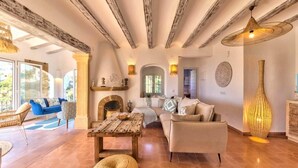 A spacious living area with a fireplace, a sofa, a dining table, and a large window. - Villa Granadella with Sea Views in Jávea, Pool & BBQ for Weekly Retreats and Families (Costa Nova)