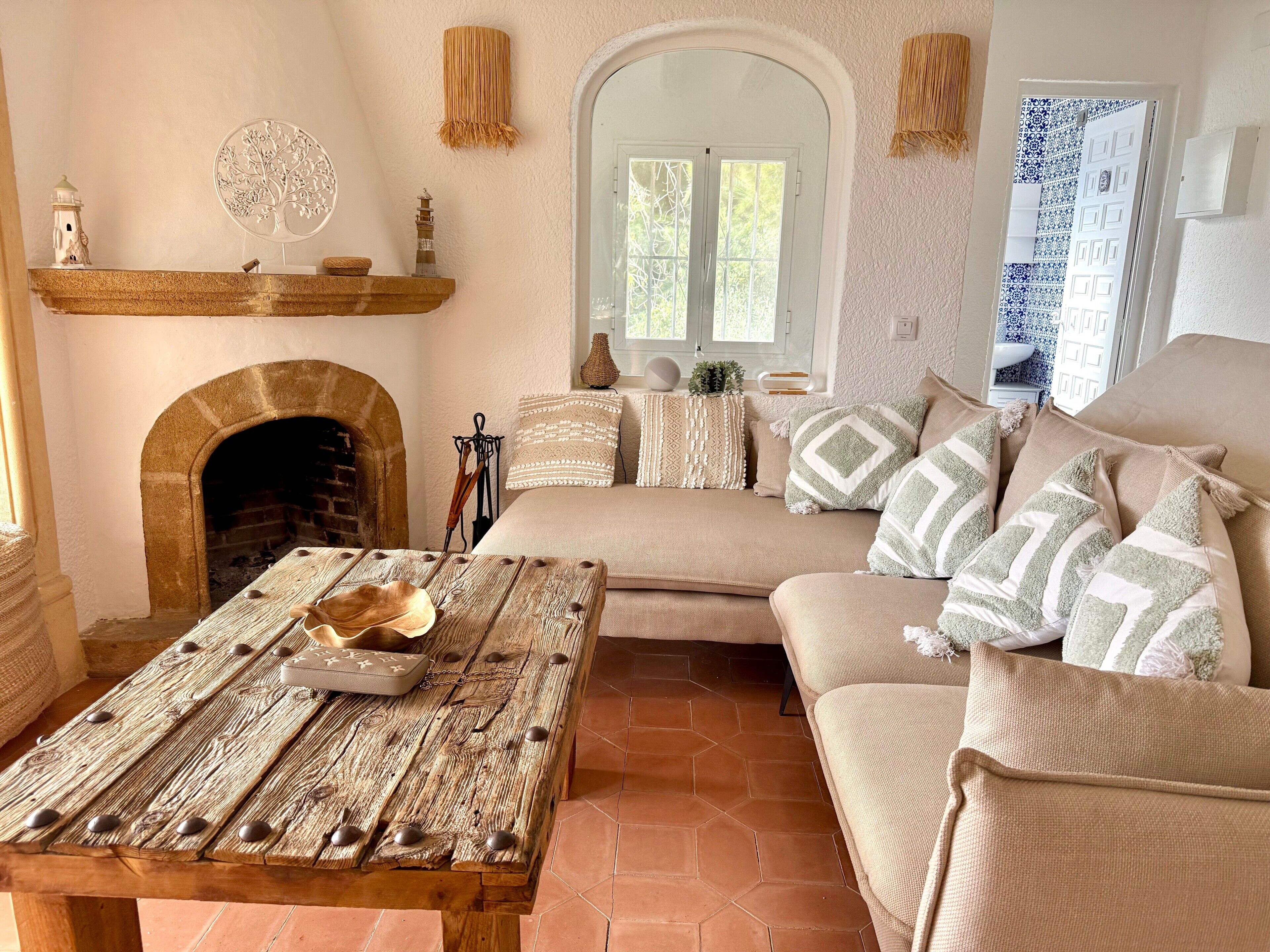 A cozy room with a fireplace, a wooden table, a sofa with patterned cushions, and a decorative wall piece.