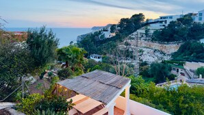 A coastal view with a wooden deck, a white building, and a cliff with vegetation. - Villa Granadella with Sea Views in Jávea, Pool & BBQ for Weekly Retreats and Families (Costa Nova)