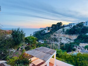 A coastal view with a wooden deck, a white building, and a cliff with vegetation. - Villa Granadella with Sea Views in Jávea, Pool & BBQ for Weekly Retreats and Families (Costa Nova)
