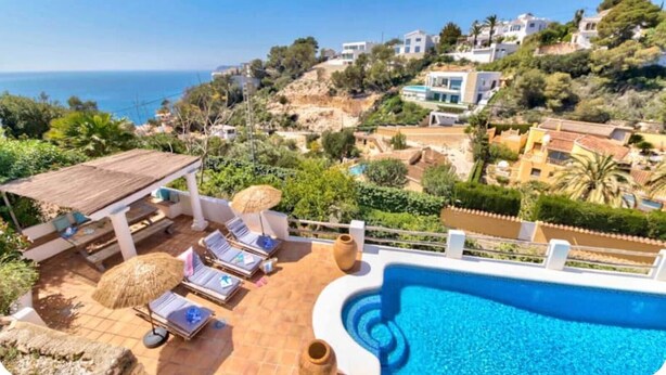 A rooftop pool with lounge chairs, a pergola, and a view of the sea and hillside houses. - Villa Granadella with Sea Views in Jávea, Pool & BBQ for Weekly Retreats and Families (Costa Nova)