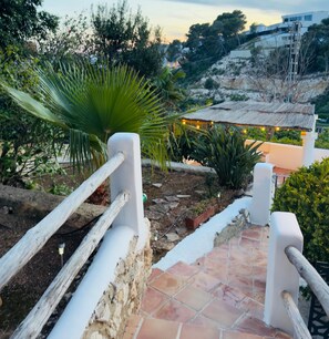 A staircase leading to a terrace with a thatched roof, surrounded by greenery and a view of a hillside. - Villa Granadella with Sea Views in Jávea, Pool & BBQ for Weekly Retreats and Families (Costa Nova)