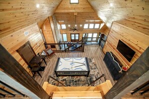 A wooden cabin interior with a dining area, a fireplace, a television, and a staircase. - Cozy Cabin with Hot Tub & Fireplace in Broken Bow, Oklahoma (Broken Bow)