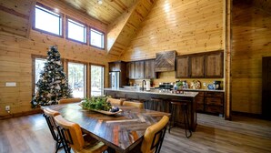 A wooden interior with a dining table, chairs, a Christmas tree, and a kitchen area. - Cozy Cabin with Hot Tub & Fireplace in Broken Bow, Oklahoma (Broken Bow)