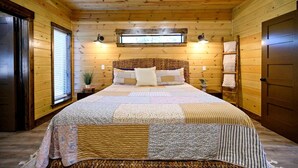 A wooden-paneled bedroom with a bed, two bedside lamps, a window, and a door. - Cozy Cabin with Hot Tub & Fireplace in Broken Bow, Oklahoma (Broken Bow)
