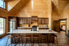 A spacious kitchen with wooden walls, a large island with bar stools, and a stainless steel refrigerator. - Cozy Cabin with Hot Tub & Fireplace in Broken Bow, Oklahoma (Broken Bow)