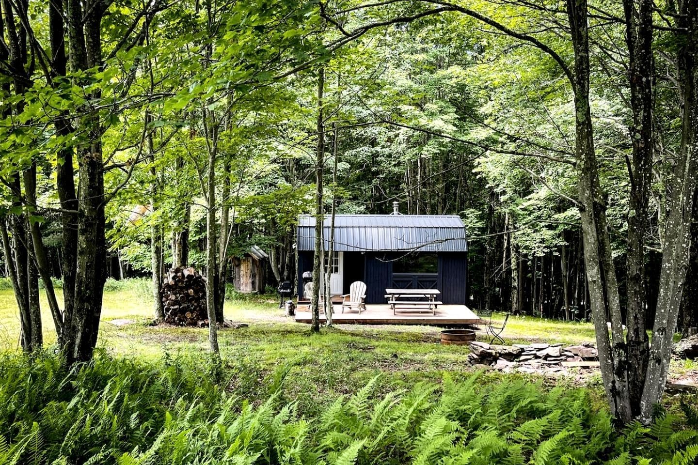 A cabin in a forest with a deck, a chair, and a table.