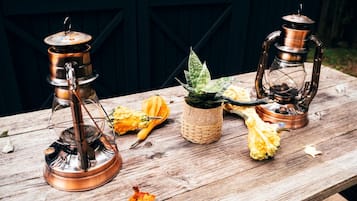 Uma mesa de madeira rústica com duas lanternas de cobre, um vaso de planta e abóboras.