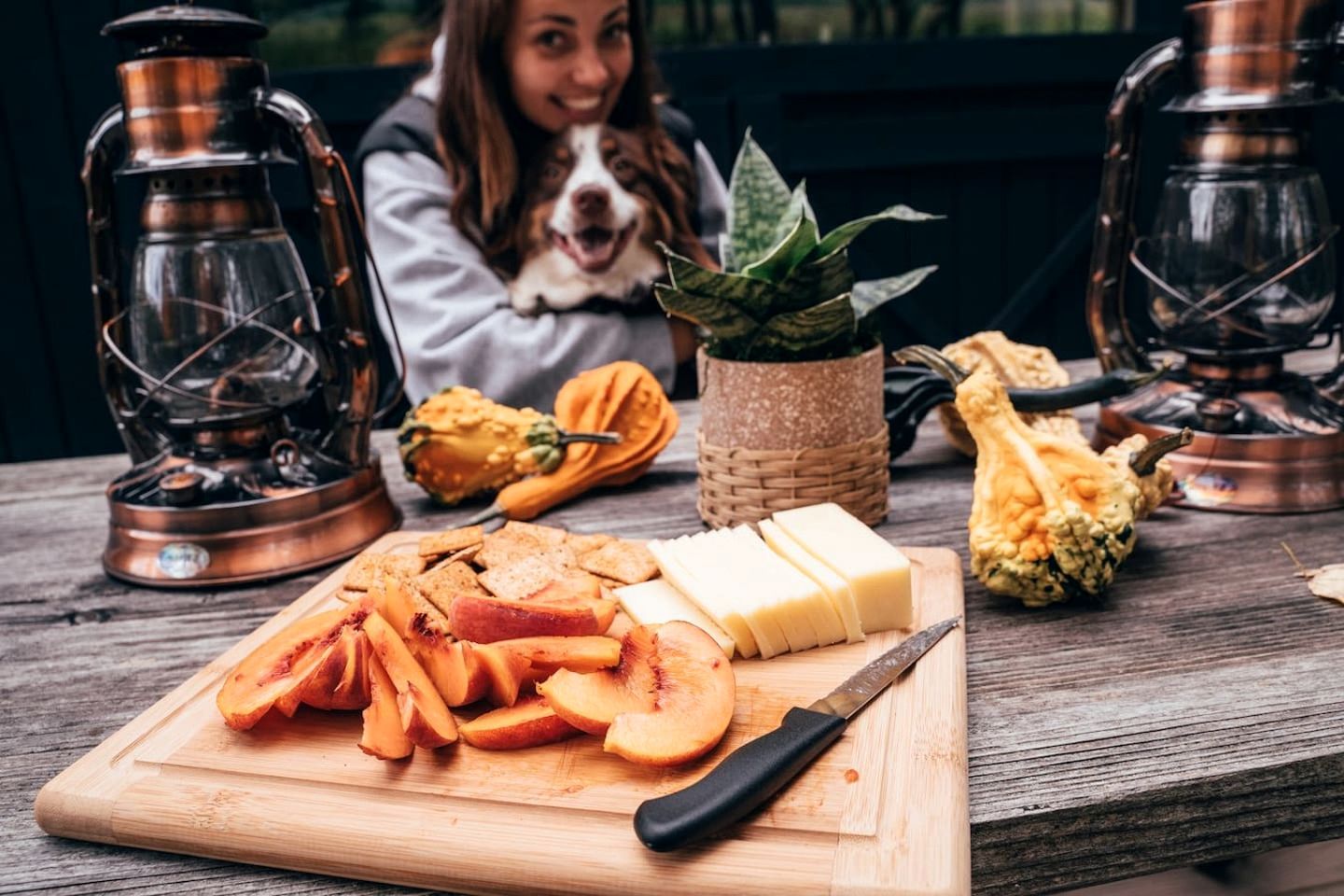 Una tabla de madera con frutas cortadas, un cuchillo y una botella de mantequilla sobre una mesa.