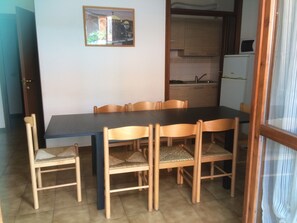 A dining area with a table and chairs, a kitchen in the background, and a framed picture on the wall. - Da Elena Apartment, two-room apartment with private garden, complex with pool and tennis court (Pacengo)