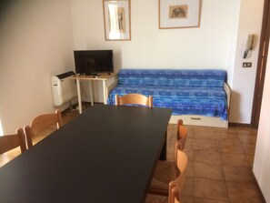 A dining area with a table, chairs, a television, and a sofa. - Da Elena Apartment, two-room apartment with private garden, complex with pool and tennis court (Pacengo)
