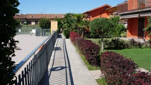 A pathway leading to a building with a balcony, surrounded by greenery and a clear sky. - Da Elena Apartment, two-room apartment with private garden, complex with pool and tennis court (Pacengo)